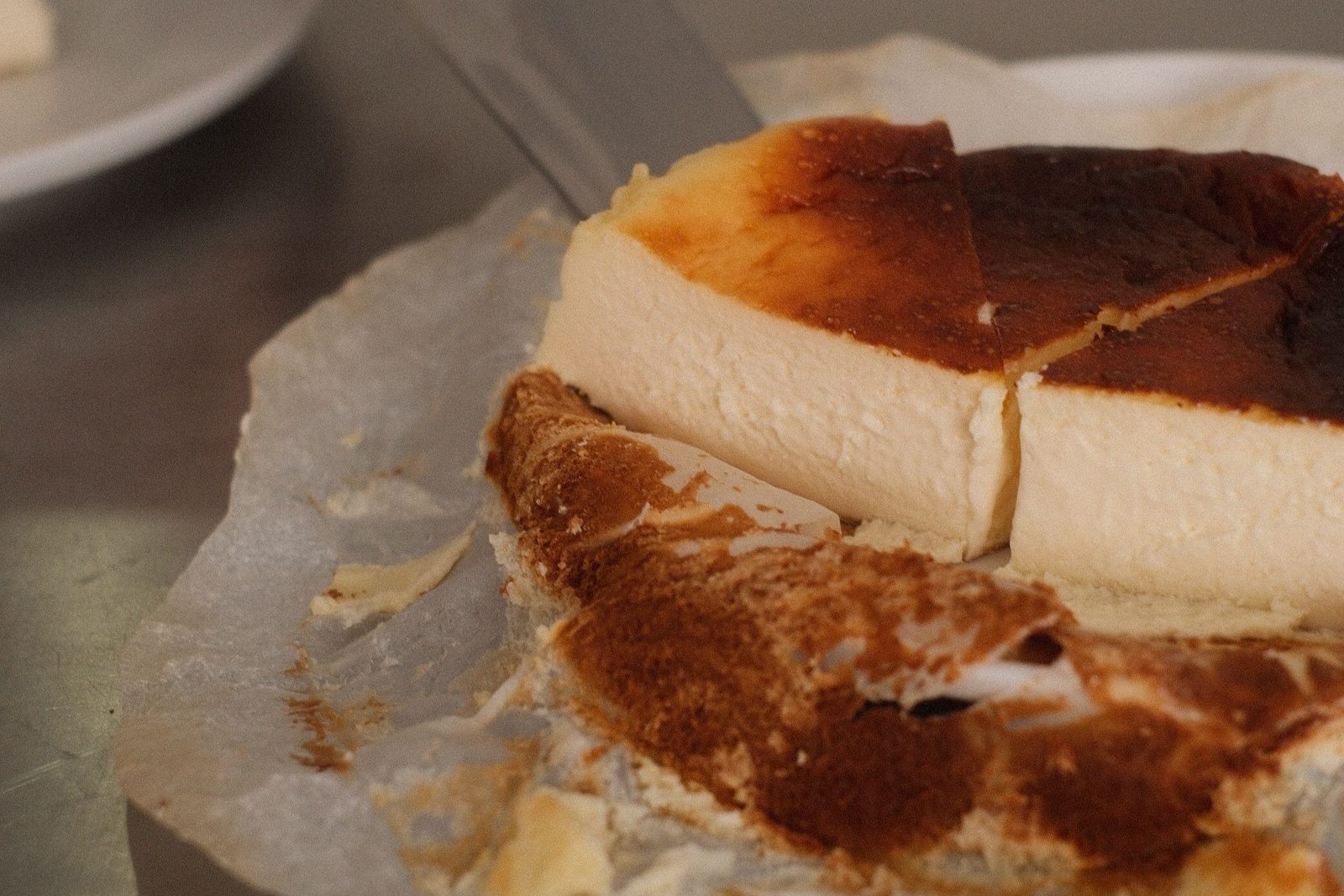 A Basque cheesecake with a caramelized top being cut in its parchment