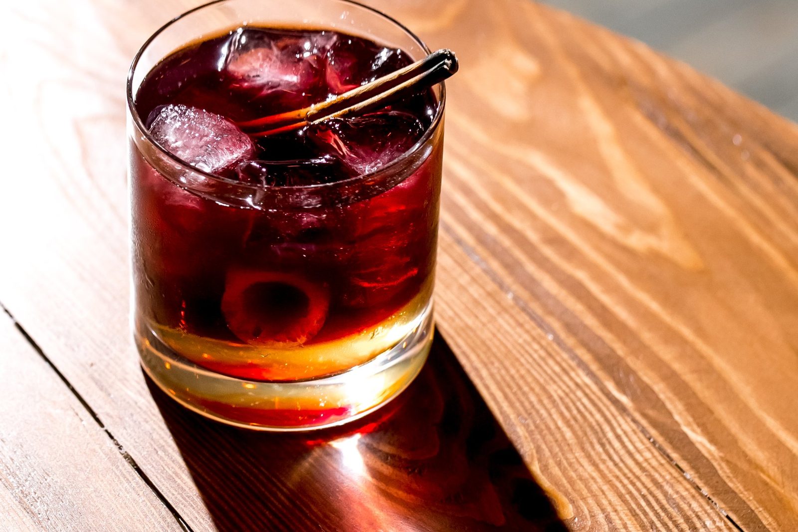 A glass of red vermouth on ice on a wooden bar table